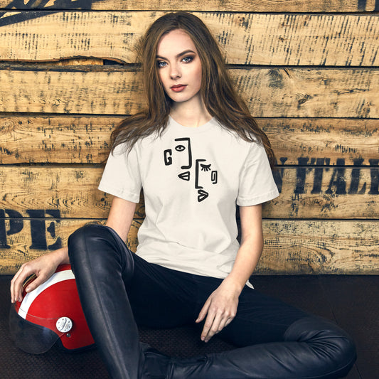 Woman wearing a white t-shirt with a graphic design, sitting against a wooden wall.