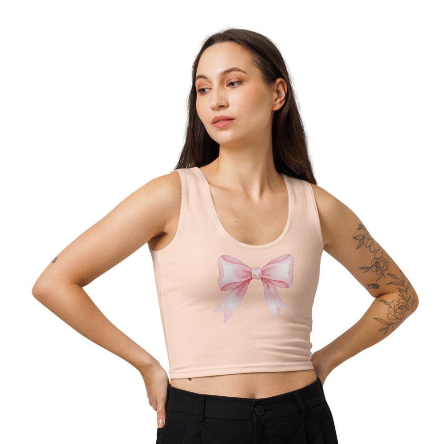 Woman wearing a beige tank top with a bow ribbon design and black pants on a white background