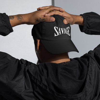Person wearing a black cap with 'SAVAGE' hands on head, against a neutral background