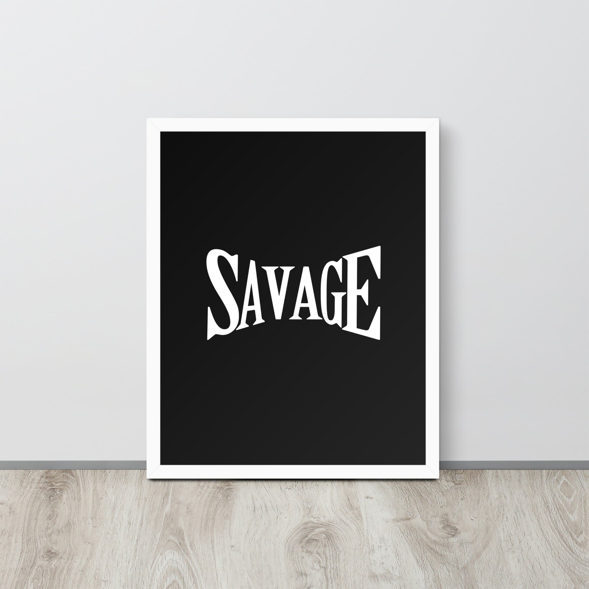 Framed poster with the word 'SAVAGE' on a black background, placed on a wooden surface with a light gray wall in the background.