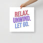 Hand holding a sign with 'Relax. Unwind. Let Go.' text on a plain background