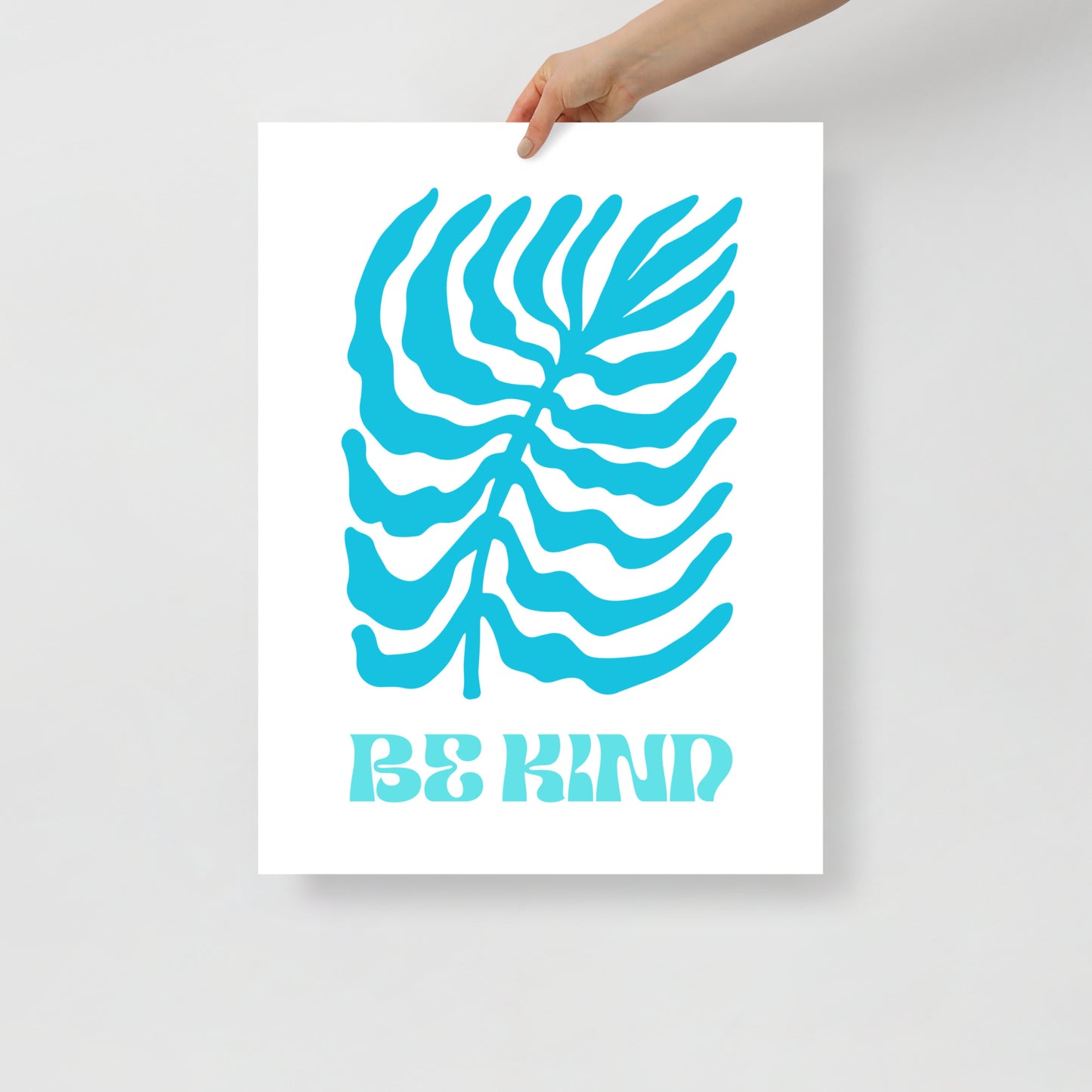 Poster with blue leaf design and 'Be Kind' text held by a hand on a light gray background