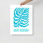 Poster with blue leaf design and 'Be Kind' text held by a hand on a light gray background