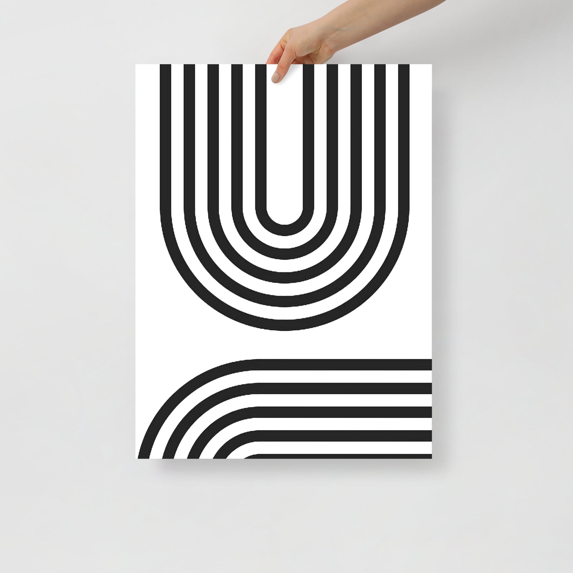 Poster with black and white geometric design held by a hand on a light gray background