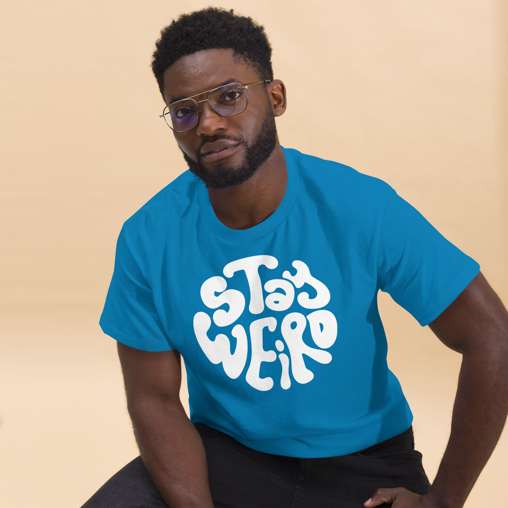 Man wearing a blue t-shirt with 'Stay Weird' text on a beige background