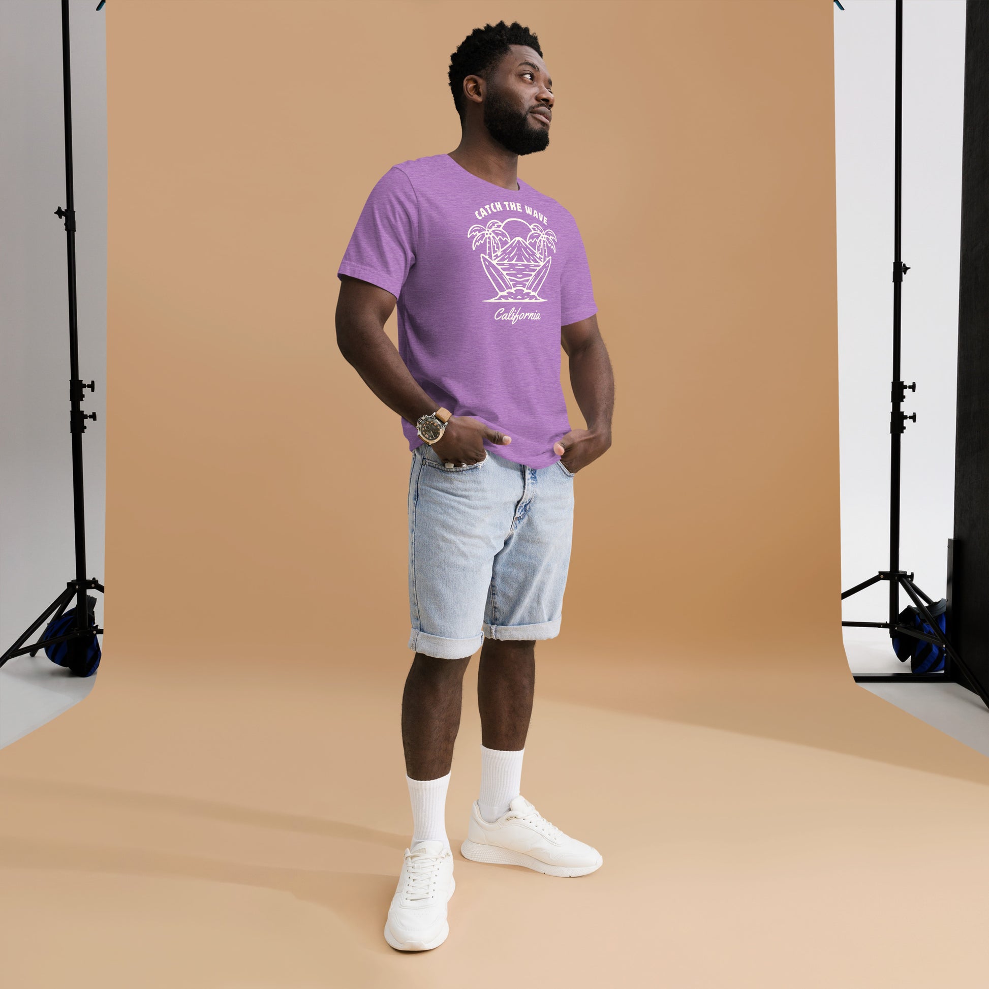 Man wearing a purple t-shirt with a logo and light blue shorts standing against a brown backdrop.